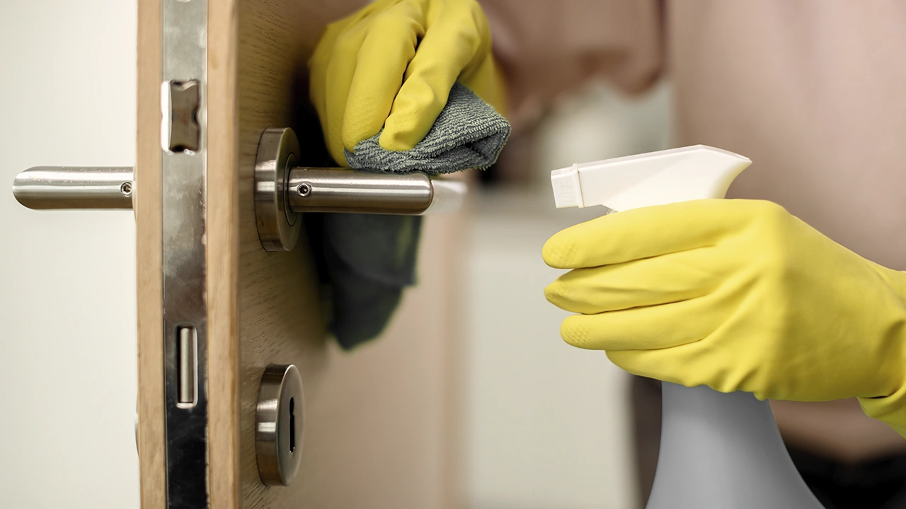 Gloved hand disinfecting a door handle during a deep cleaning