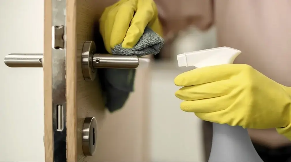 Gloved hand spraying and wiping a door handle during a deep cleaning